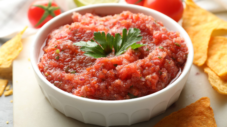 A small dish of salsa with tortilla chips on a platter