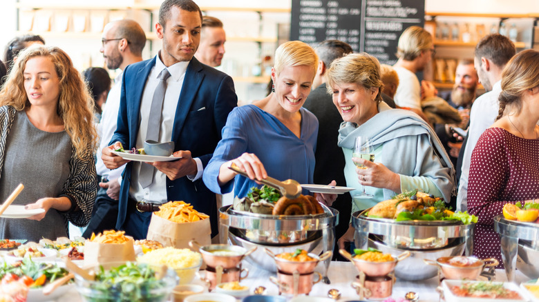People enjoying a buffet. Buffet table with variety dishes at social event. Happy diverse people chatting and enjoy with food and drink. Buffet table with social gathering, diverse crowd, buffet.