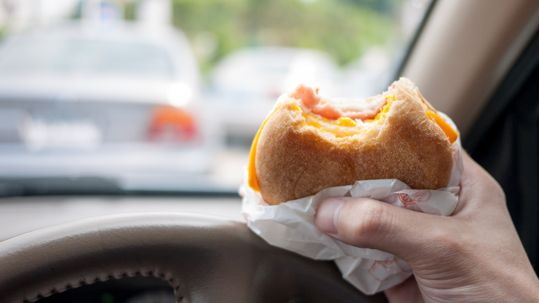 Person's hand holding up a fast food breakfast sandwich in their car with traffic in the background.