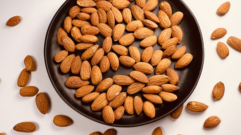 Almonds in shallow black bowl on white tabletop surface.