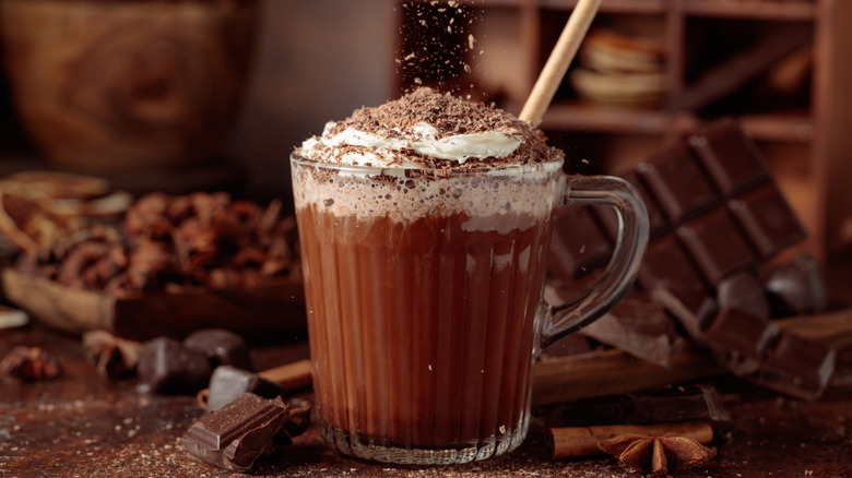 Glass mug filled with hot chocolate, topped with whipped cream, and chocolate shavings