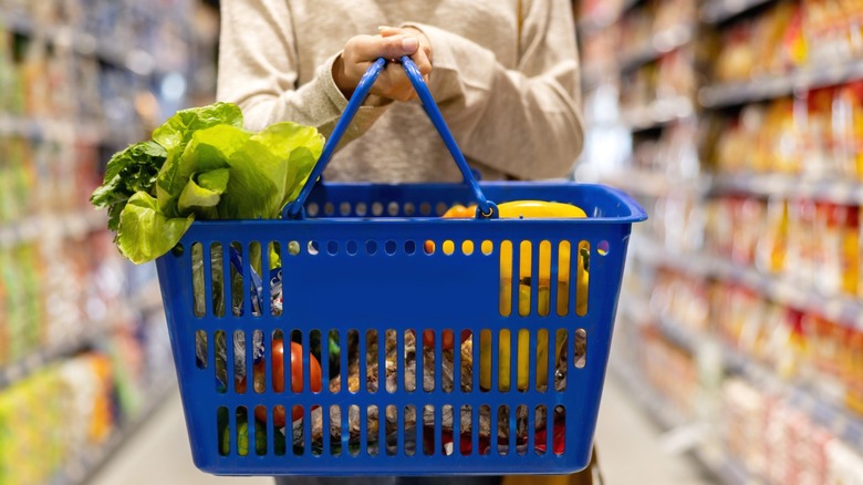 A woman at the supermarket walking the aisles holding her basket.