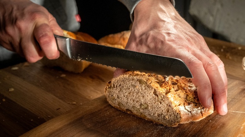 Person cutting loaf of bread on wood board with bread knife