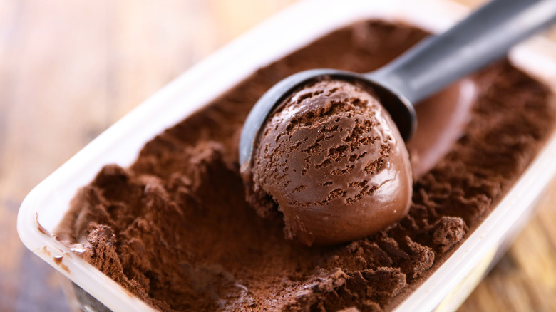 Dark chocolate ice cream in container with metal ice cream scooping in