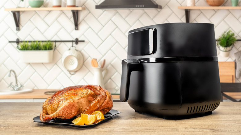A whole roasted chicken on a plate next to a black air fryer on a kitchen counter