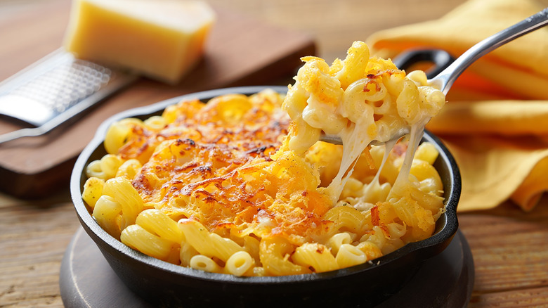 Mac and cheese in a cast iron skillet with a cheese pull by a fork