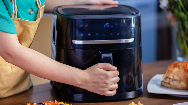 A person wearing an apron using an air fryer to prepare food in the kitchen.