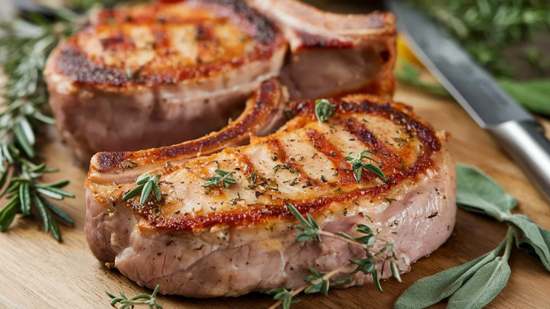 Seared bone-in pork chops on a wooden chopping board with sprigs of thyme