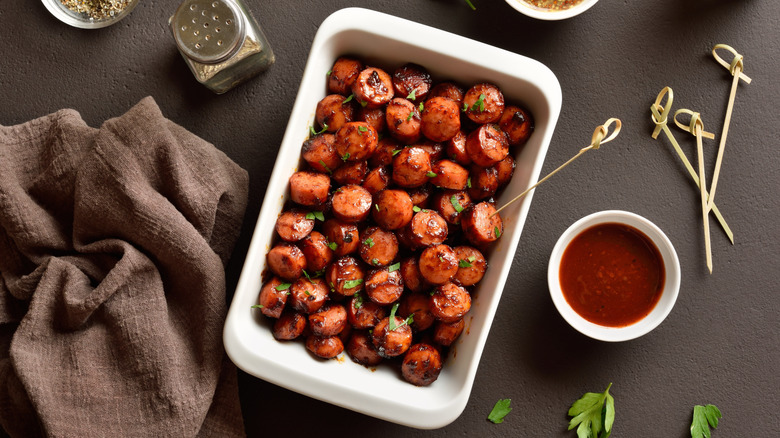 Sweet and spicy air fryer smoked sausage bites in white baking dish on brown stone background. Top view, flat lay