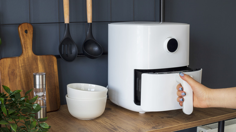 Someone opening a white air fryer on a wooden kitchen counter.