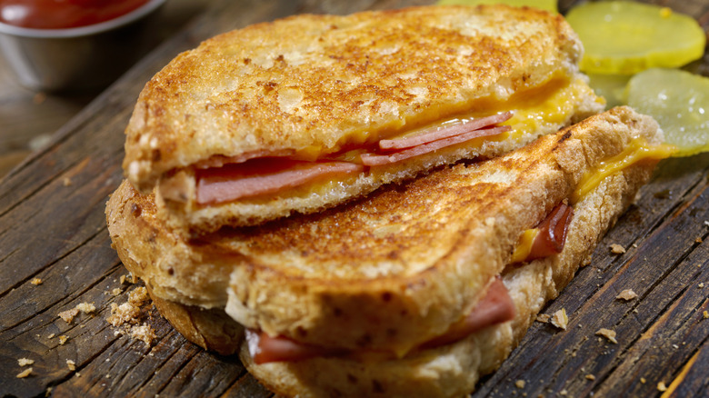 A grilled cheese with fried bologna and pickles in the background.