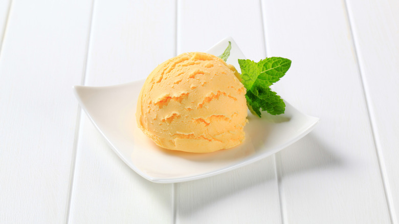 A scoop of orange ice cream served on a white plate