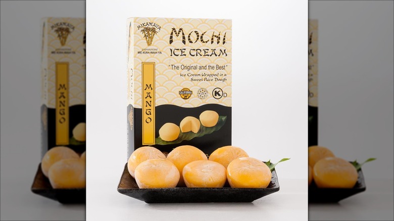 Six mango mochi ice cream pieces on a black plate on display in front of a box of Mikawaya Mochi Ice Cream