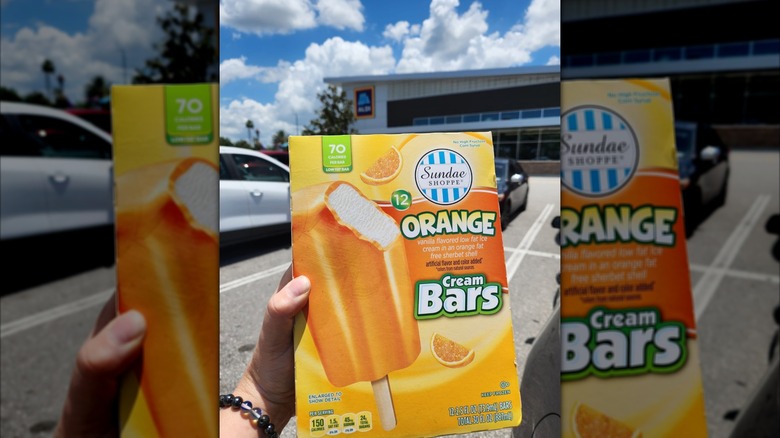 A hand holds a box of Aldi's Sundae Shoppe Orange Cream Bars in a supermarket parking lot