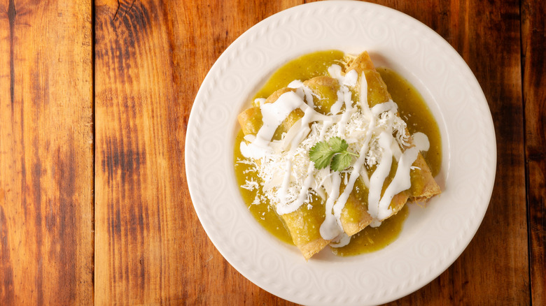 Top view of enchiladas in salsa verde topped with sour cream and cheese