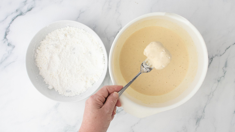 Bowl of cornstarch next to hand dunking nugget into bowl of batter