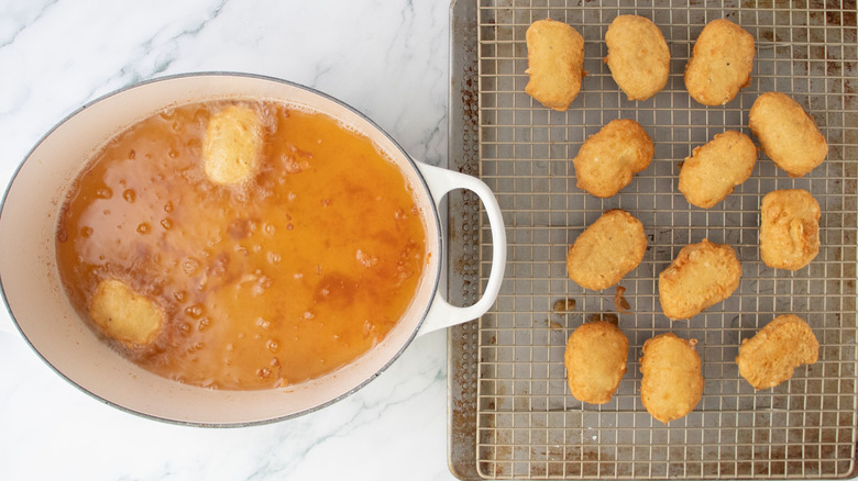 Chicken nuggets frying in large pot next to nuggets on wire rack