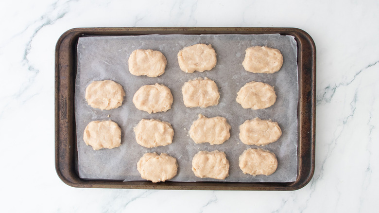 Raw chicken nuggets on baking sheet