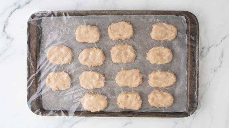 Raw chicken nuggets on baking sheet covered with plastic