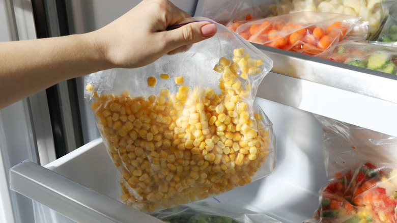 Hand pulling bag of frozen corn from freezer