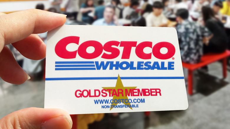 Hand holding a Costco membership card inside a Costco store