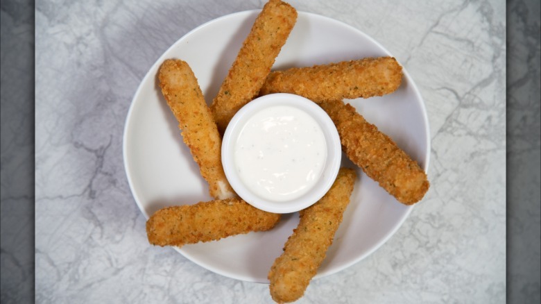 Mozzarella sticks arranged on white plate with small bowl of ranch dressing