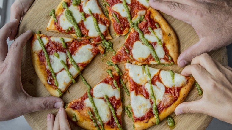hands reaching for pizza slices garnished with Kirkland Signature pesto
