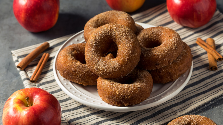 Apple cider donuts stacked on top of plate with apples and spices near