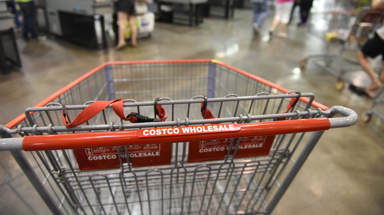 An empty Costco shopping cart with people's legs in the background inside the store.