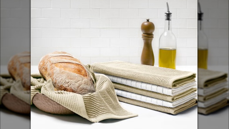 Loaf of bread in a towel-lined basket next to a pile of kitchen towels