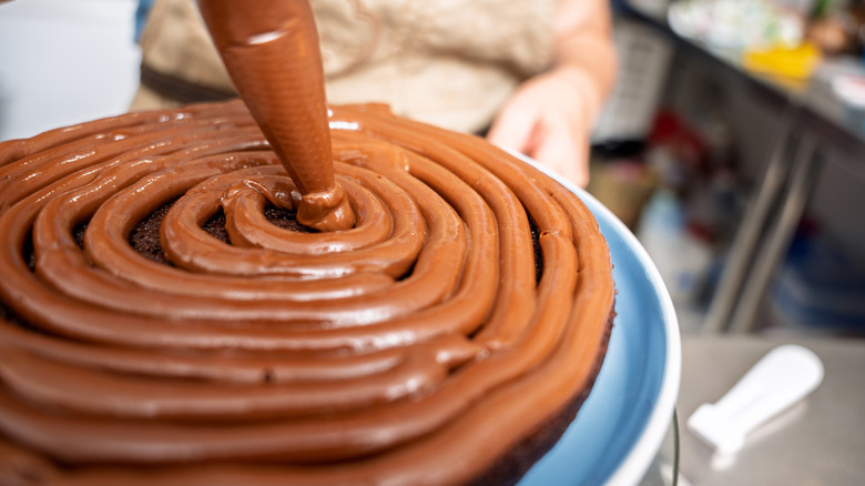 baker piping chocolate filling onto a chocolate cake