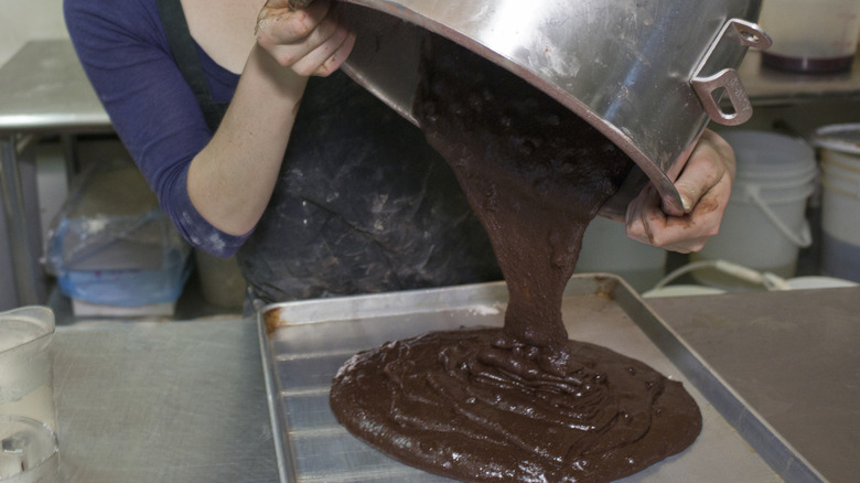 baker pours chocolate cake batter into sheet tray