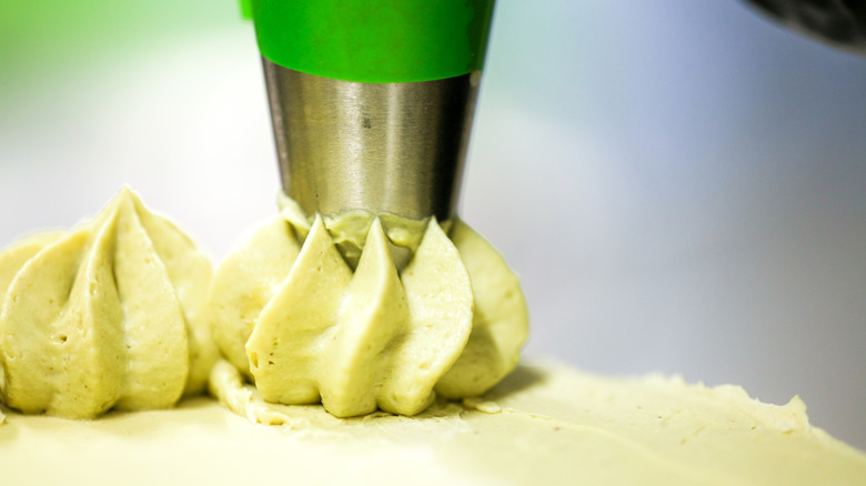 a green piping bag with a silver tip dollops light green frosting on a cake