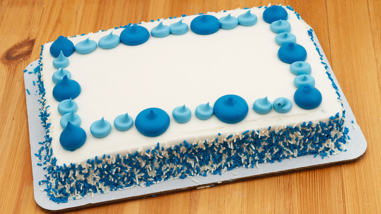 sheet cake with white and blue icing and sprinkles on a wooden surface