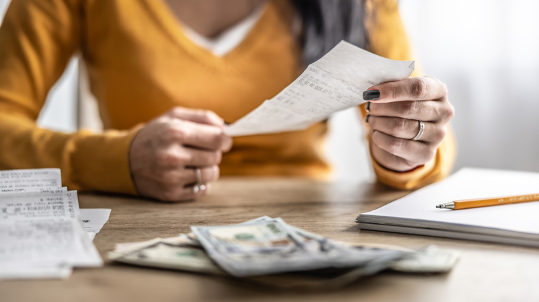 woman in yellow shirt reviews receipt with notepad and cash on table in front of her