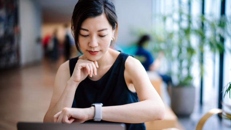 woman in black tank top looks down at digital watch