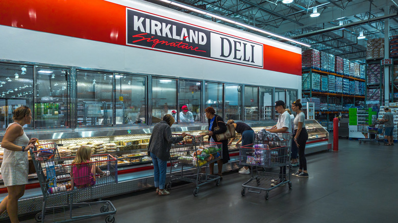 People shopping in the Kirkland Signature Deli section of a Costco store.