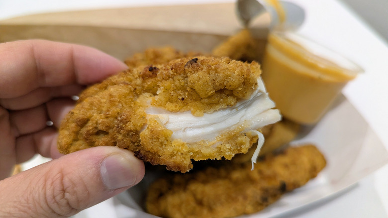 Hand holding torn open chicken tender exposing meat.