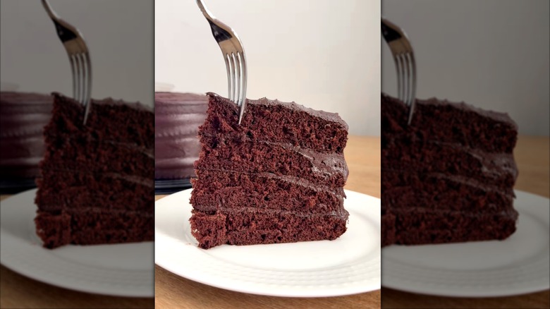Sticking a fork into a slice of Costco's Chocolate Fudge Cake on a white plate