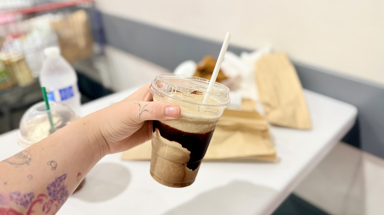 Hand holding a frozen Costco frappe with chocolate syrup in plastic takeout cup with straw
