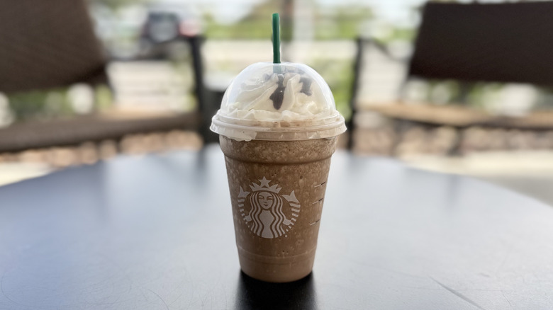 Starbucks Mocha Frappuccino topped with whipped cream in plastic takeout cup on table with straw