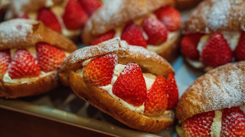 Sweet, powdered sugar buns with cream filling and strawberries on a tray.