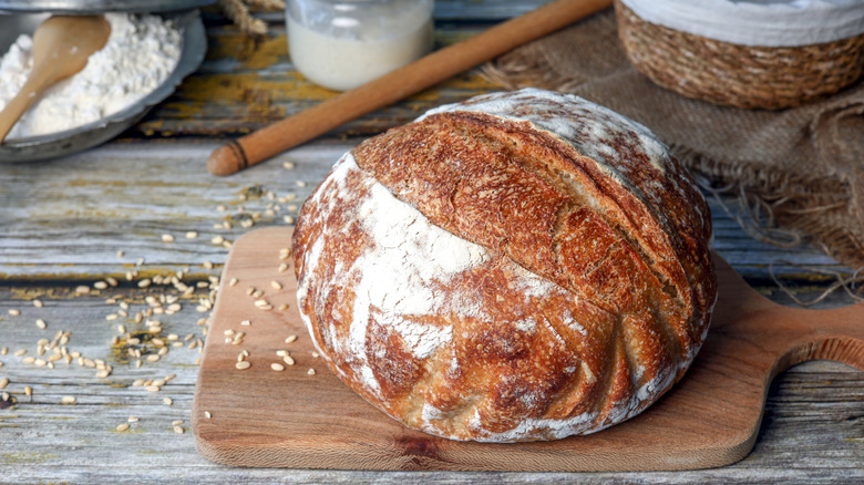 Homemade sourdough bread loaf sitting on a wood bread board on a farmhouse table.