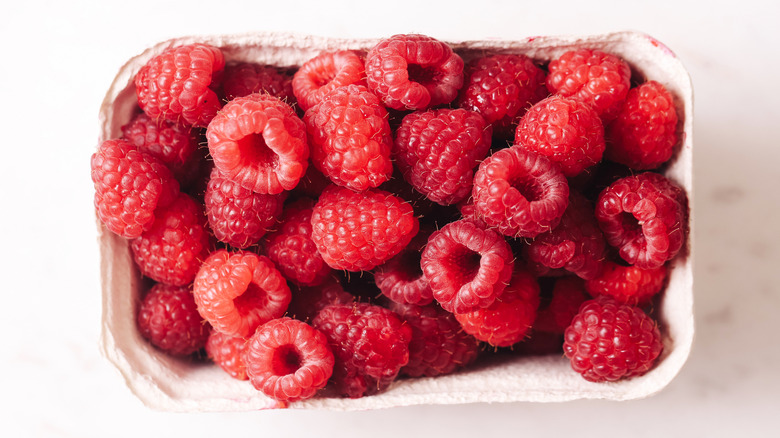 Raspberries in cardboard carton on countertop.