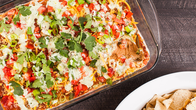 Top view of seven layer dip in glass pan alongside tortilla chips