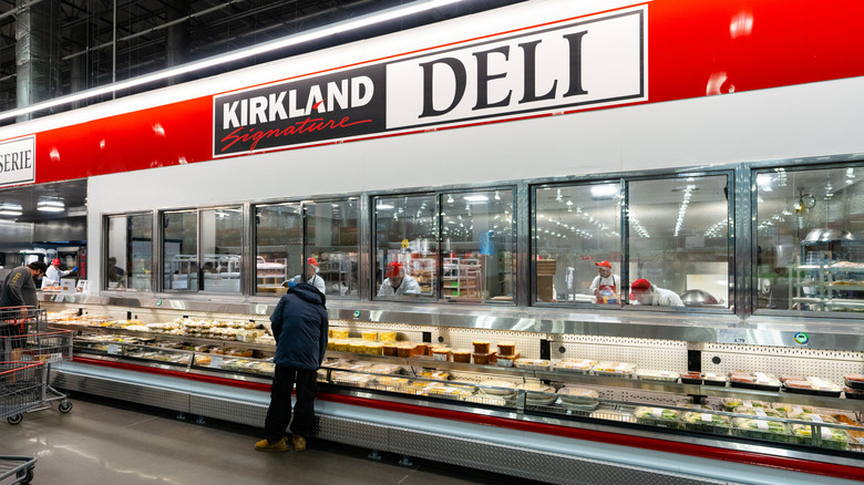 A Costco Deli section with a customer standing over the food picking something out.