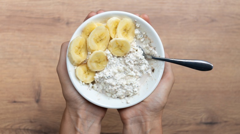 Hands holding a bowl of cottage cheese and banana slices