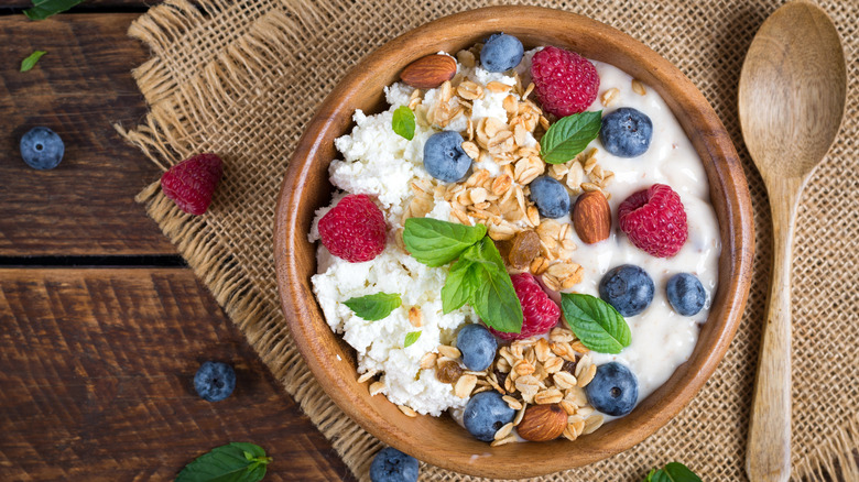 A wooden bowl filled with cottage cheese on one side and greek yogurt on the other, separated by granola and berries