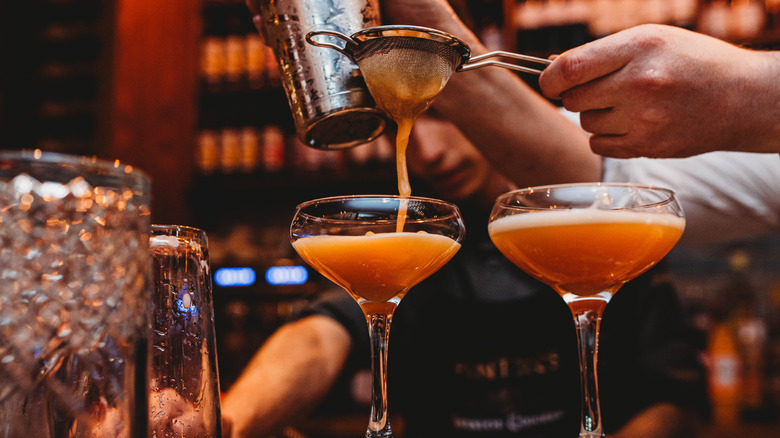 A bartender strains juice into a martini