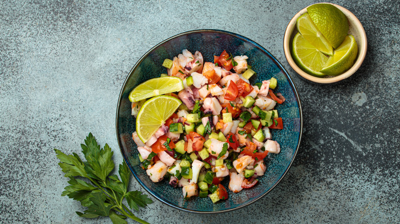 ceviche in a green bowl with lime wedges and cilantro on the side